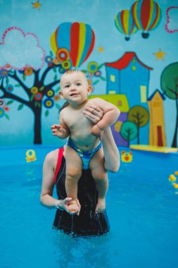 Bir çocuk bir koçla havuzda yüzmeyi öğrenir. Çocuklara yüzmeyi öğretmek..