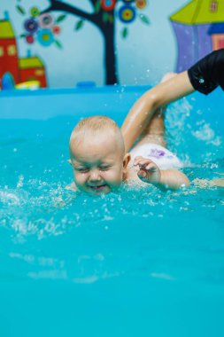 Çocuk bir yıldır havuzda bir koçla birlikte yüzüyor. Bir çocuğa yüzmeyi öğretmek. Çocuklar için yüzme havuzu.