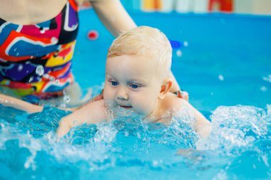 Havuzdaki bir erkek bebek koçla yüzmeyi öğreniyor. Çocuklara yüzme öğretmek için yüzme havuzu