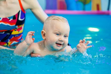 Bir bebek bir antrenörle havuzda yüzmeyi öğrenir. Çocuk havuzu. Çocuklar için yüzme kursları.