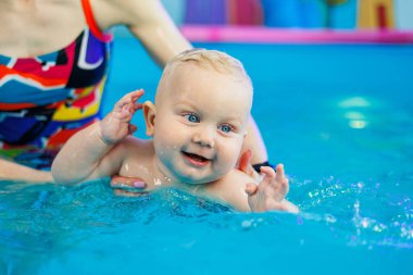 Bir bebek bir antrenörle havuzda yüzmeyi öğrenir. Çocuk havuzu. Çocuklar için yüzme kursları.
