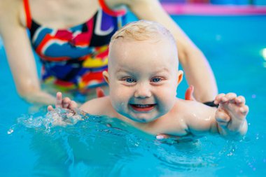 Küçük bir çocuk bayan bir koçla havuzda yüzmeyi öğreniyor. Bebek havuzda yüzüyor..
