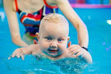 Küçük bir çocuk bayan bir koçla havuzda yüzmeyi öğreniyor. Bebek havuzda yüzüyor..