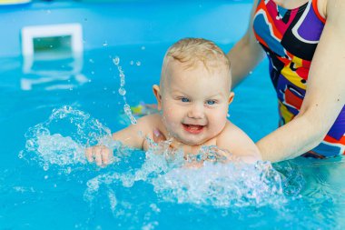 Küçük bir çocuk bayan bir koçla havuzda yüzmeyi öğreniyor. Bebek havuzda yüzüyor..