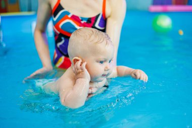 Erkek çocuk havuzda yüzüyor. Bir antrenör bebeğe yüzmeyi öğretir..