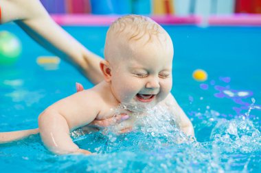 Erkek çocuk havuzda yüzüyor. Bir antrenör bebeğe yüzmeyi öğretir..