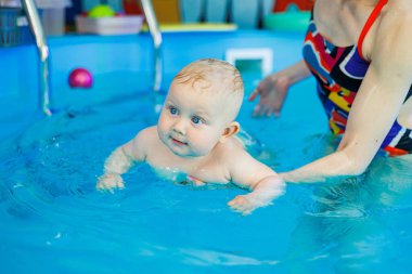 Erkek çocuk havuzda yüzüyor. Bir antrenör bebeğe yüzmeyi öğretir..