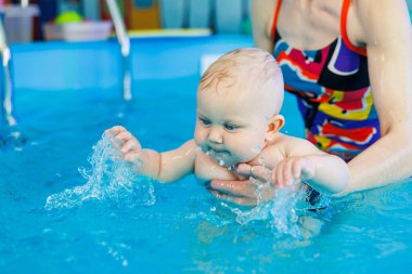 Erkek çocuk havuzda yüzüyor. Bir antrenör bebeğe yüzmeyi öğretir..