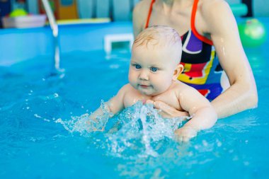 Erkek çocuk havuzda yüzüyor. Bir antrenör bebeğe yüzmeyi öğretir..