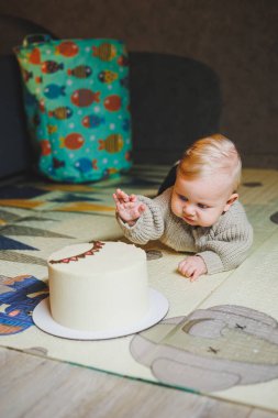 Sarışın bir bebek evde yerde sürünüyor ve tatlı bir pasta yemek istiyor. Çocuk gelişimi. Bir çocuk emeklemeyi öğrenir.
