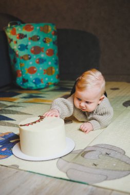 Sarışın bir bebek evde yerde sürünüyor ve tatlı bir pasta yemek istiyor. Çocuk gelişimi. Bir çocuk emeklemeyi öğrenir.