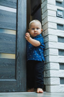 Evdeki sarışın çocuk, kapıdaki bir çatlaktan odaya gizlice bakıyor. Çocuk 1 yaşında. Odanın kapısını açıyor. Evdeki çocuklar.