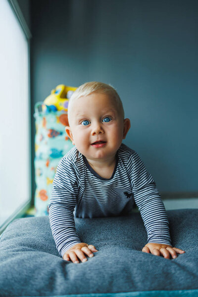 Blond baby crawling on the floor at home. Child development. Boy learning to crawl.