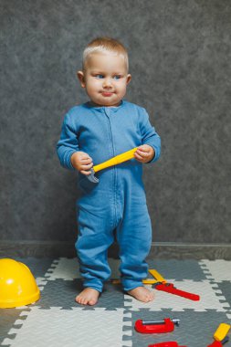 1 yaşındaki çocuk mavi tulumlu evde oyuncaklarla oynuyor. Oturma odasında. Çocuğun kendi kendini geliştirmesi. Bebekler için oyuncaklar.