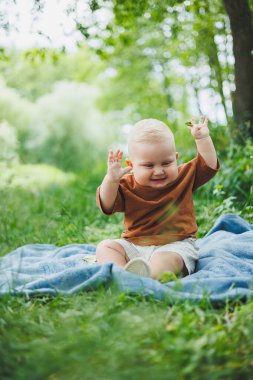 Küçük çocuk 1 yaşında parkta çimlerin üzerinde oturmuş ekmek yiyor. Bebek temiz havada yürüyüşe çıktı..