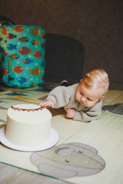 Sarışın bir bebek evde yerde sürünüyor ve tatlı bir pasta yemek istiyor. Çocuk gelişimi. Bir çocuk emeklemeyi öğrenir.