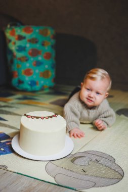 Sarışın bir bebek evde yerde sürünüyor ve tatlı bir pasta yemek istiyor. Çocuk gelişimi. Bir çocuk emeklemeyi öğrenir.