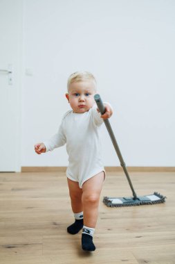 Küçük çocuk yerleri paspasla yıkıyor. Yeni yürümeye başlayan çocuk evde temizlik yapıyor. Daireyi temizlemek için paspas..