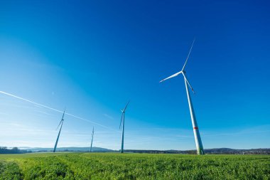 Rüzgar enerjisi üretimi. Elektrik, mavi gökyüzüne karşı bir rüzgar türbini tarafından üretilir. Rüzgarlı yeşil bölgede sürdürülebilir enerji üretimi. Ekolojik enerji üretimi