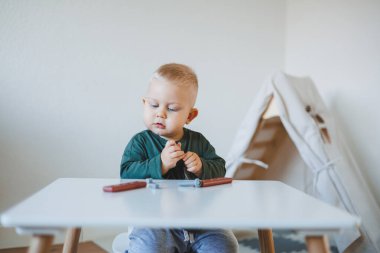 Küçük çocuk parlak bir odada çocuk masasında oturup oyuncaklarla oynuyor. Çocuklar için mobilya. Bebekler için masa ve sandalyeler. Çocuk gelişimi