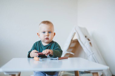 Küçük çocuk parlak bir odada çocuk masasında oturup oyuncaklarla oynuyor. Çocuklar için mobilya. Bebekler için masa ve sandalyeler. Çocuk gelişimi