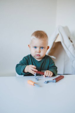 Küçük çocuk parlak bir odada çocuk masasında oturup oyuncaklarla oynuyor. Çocuklar için mobilya. Bebekler için masa ve sandalyeler. Çocuk gelişimi