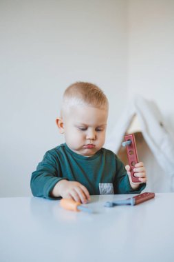Küçük çocuk parlak bir odada çocuk masasında oturup oyuncaklarla oynuyor. Çocuklar için mobilya. Bebekler için masa ve sandalyeler. Çocuk gelişimi
