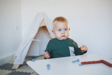 Sarışın çocuk çocuk çocuk odasında oyuncaklarla oynuyor yakın plan çekimde ve mekanı kopyalıyor. Masada taburede oturan bir çocuk. Çocuklar için mobilya