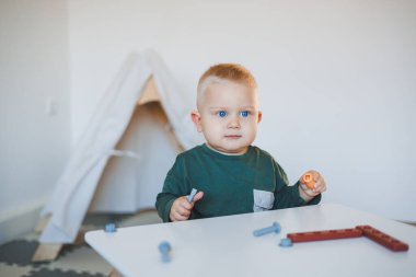 Sarışın çocuk çocuk çocuk odasında oyuncaklarla oynuyor yakın plan çekimde ve mekanı kopyalıyor. Masada taburede oturan bir çocuk. Çocuklar için mobilya
