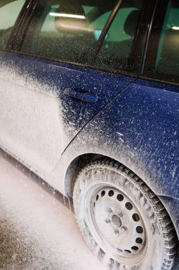 Oto yıkamada kimyasallarla yıkanmak, kirli mavi bir araba için beyaz köpük..