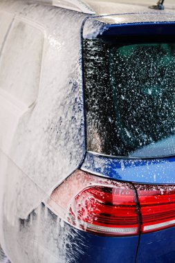 Kirli araba yoğun köpükle kaplı. Otomobil yıkamada mavi araba.