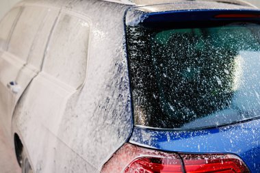 Kirli araba yoğun köpükle kaplı. Otomobil yıkamada mavi araba.