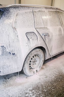 Kirli araba yoğun köpükle kaplı. Otomobil yıkamada mavi araba.