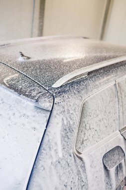 Kirli araba yoğun köpükle kaplı. Otomobil yıkamada mavi araba.