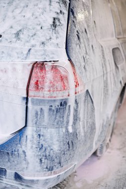 Kirli araba yoğun köpükle kaplı. Otomobil yıkamada mavi araba.