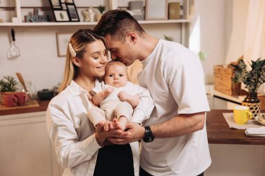 Happy family with newborn son playing in the kitchen. Family couple at home with son making coffee in the kitchen. Home family atmosphere clipart