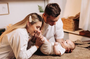 Smiling young family with child, father and mother with little baby, newborn child, having morning breakfast in home kitchen. Family enjoying parenthood at home. clipart