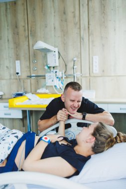 Bir adam, doğurmak üzere olan karısının elini tutar. Genç bir kadında doğumun başlangıcı. Doğum sırasındaki kocanın desteği. Doğum partneri. Doğum odası..