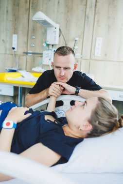 Bir adam, doğurmak üzere olan karısının elini tutar. Genç bir kadında doğumun başlangıcı. Doğum sırasındaki kocanın desteği. Doğum partneri. Doğum odası..