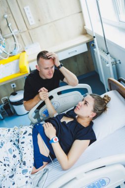 Bir adam, doğurmak üzere olan karısının elini tutar. Genç bir kadında doğumun başlangıcı. Doğum sırasındaki kocanın desteği. Doğum partneri. Doğum odası..