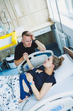 Bir adam, doğurmak üzere olan karısının elini tutar. Genç bir kadında doğumun başlangıcı. Doğum sırasındaki kocanın desteği. Doğum partneri. Doğum odası..