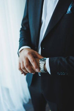 Pürüzsüz siyah takım elbiseli bir adam lüks kol saatini dikkatlice ayarlar. Hem cazibesini hem de inceliğini somutlaştırır.