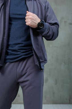 Bileğinde şık bir siyah saat ve kıyafetini tamamlayan şık gri bir ceket olan bir adam görülüyor.