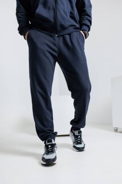 Rahat bir kapüşonlu ve sıradan eşofman giymiş bir adam elleri cebinde, rahat görünüyor.