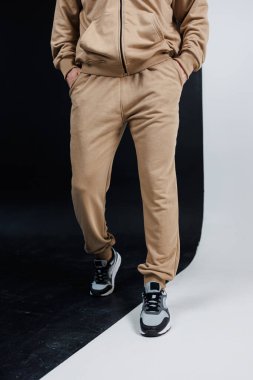 Bronzlaşmış bir ceketle uyumlu bir pantolon giyen bir adam iki eli de rahat bir şekilde cebinde duruyor.