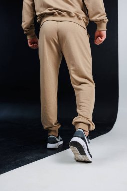 Arkadan bakıldığında, rahat bronz bir eşofman giyen bir insanın şık beyaz ayakkabılar giydiğini görüyoruz. Sıradan geziler için mükemmel.