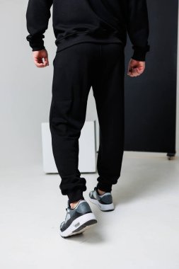 Siyah eşofman altı ve gri spor ayakkabı giyen bir adamın arka planı, çeşitli aktiviteler için rahat ama rahat bir spor tarzı sergiliyor.