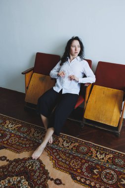 Genç bir kadın, zarif, minimalist bir iç mekan içinde rahatça poz veriyor.