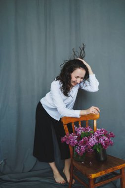 Neşeli bir kadın, rahat bir stüdyo ortamında içi canlı çiçeklerle dolu güzel bir vazoyla hoş bir şekilde etkileşime girer.