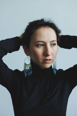 Şık, siyah bir bluz giymiş düşünceli bir kadın çarpıcı, canlı küpelerle süslenmiş zarif bir poz verir.